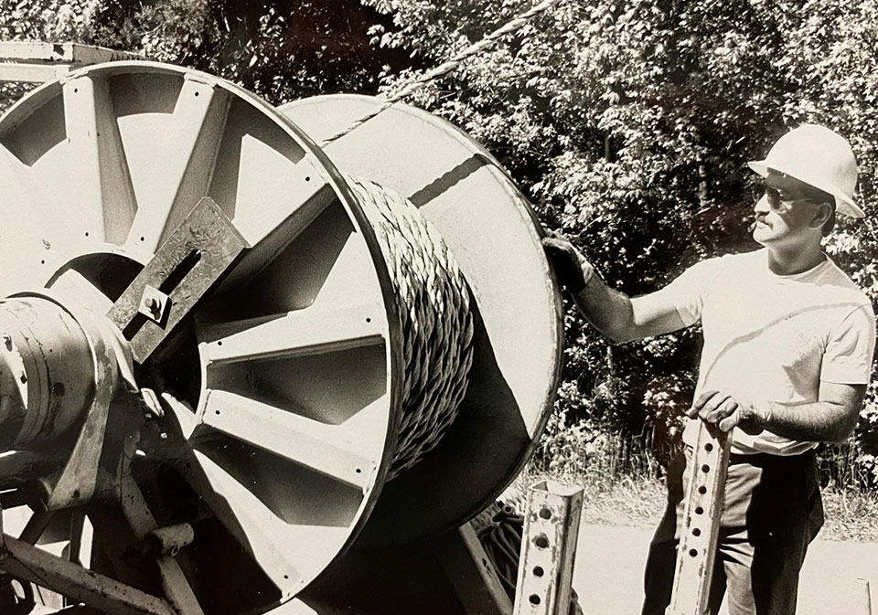 a cpw employee with a giant spool of electric line in the 70s