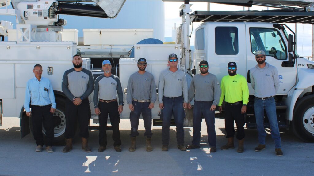 Eight linemen posing for a group photo next to a line truck.